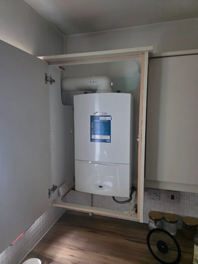 Worcester Bosch combi boiler neatly installed inside a kitchen cupboard housing with the flue routed above