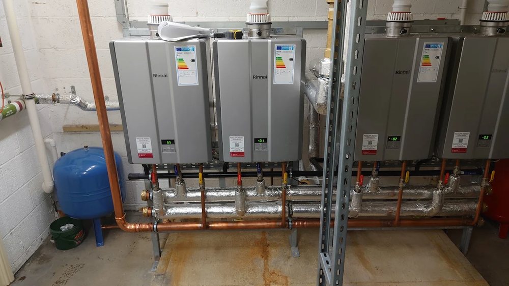 Cascade of four Rinnai commercial continuous-flow water heaters on a steel frame with insulated manifold and copper gas pipework