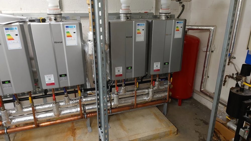 Bank of Rinnai commercial water heaters with a large red expansion vessel in a commercial plant room
