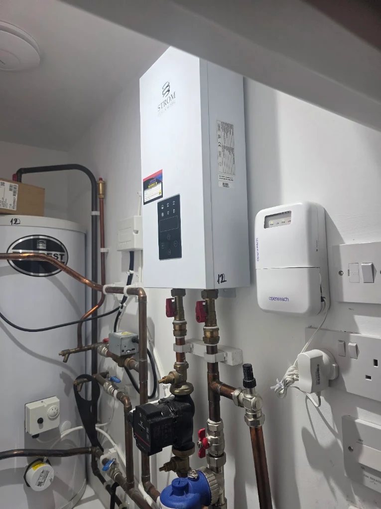 Strom electric boiler installed with circulation pump, valves, controls and copper pipework, alongside a hot water cylinder