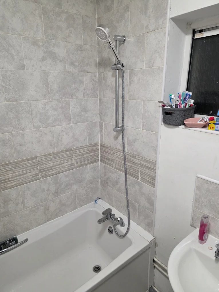 Bath with a chrome mixer tap and a shower riser rail and handset over it, tiled walls